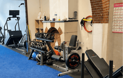 Vue de l'espace d'entraînement du cabinet mêlant équipements de fitness et mur en pierres apparentes avec cheminée